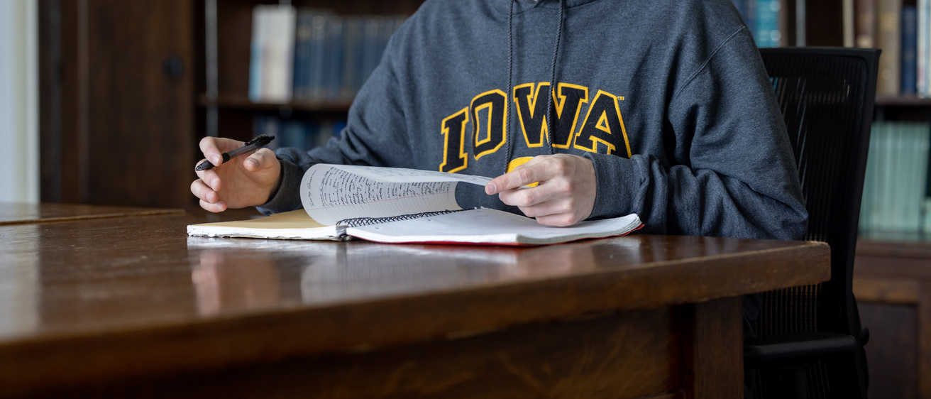 student writing in library with Iowa sweatshirt